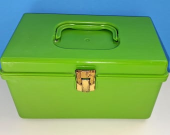 Puede incluir: Una caja de herramientas rectangular de color verde brillante con un asa en la tapa y un cierre dorado. La caja está sobre una superficie blanca con un fondo azul. La caja de herramientas mide unos 25 cm de largo.