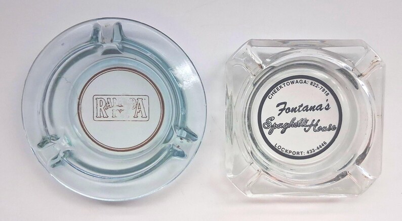 May include: Two clear glass ashtrays. The circular one features the text RAMADA in a rectangular border. The square one features the text Fontana's Spaghetti House, CHEEKTOWAGA: 822-7918, and LOCKPORT: 433-4446 printed in a circular black border.