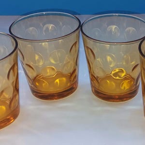 Op de afbeelding: Vier amberkleurige drinkglazen met een gestructureerd, gestippeld patroon. De glazen hebben een licht schuine rand en een afgeronde bodem. De glazen zijn gemaakt van helder glas en zijn geschikt voor het serveren van dranken.