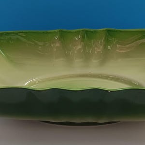 May include: A rectangular ceramic serving bowl with a lettuce leaf design. The bowl features a gradient of green hues, transitioning from a dark green base to lighter shades at the rim. The rim has a scalloped edge.
