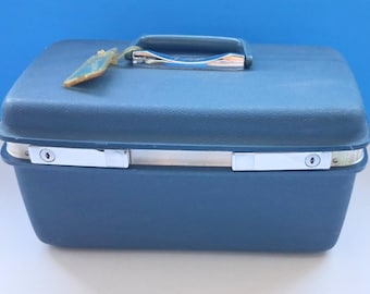 May include: A vintage navy blue travel case with a silver handle and latches. The case has a rectangular shape with rounded corners and a matching navy blue handle. A small tag hangs from the handle.