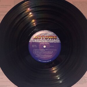 May include: A black vinyl record with the label "MOTOWN" and the artist "LIONEL RICHIE." The record is labeled "Side Two" and lists song titles including "Round and Round" and "Truly." The record is on a pink background.