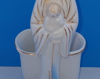 Op de afbeelding: Een witte keramische religieuze figuur die een kind vasthoudt. De figuur heeft gouden accenten en blauwe details op de basis. De achtergrond is effen blauw.