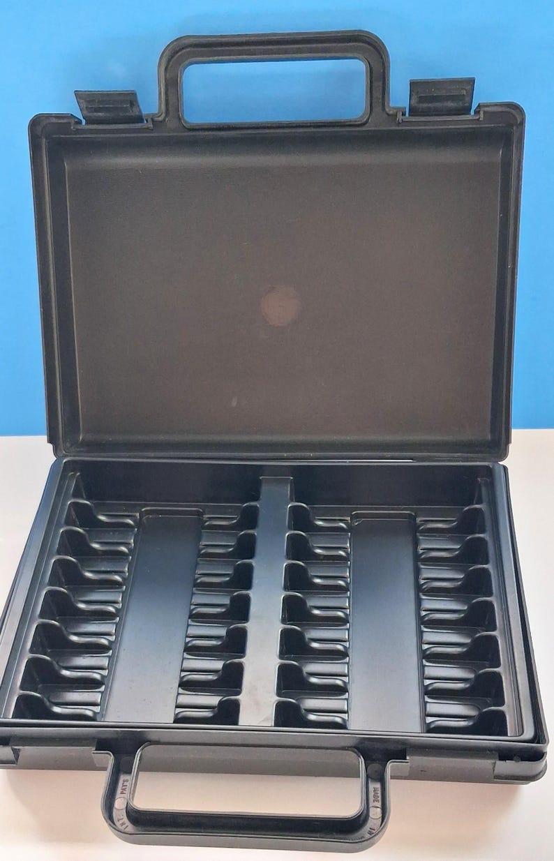 May include: An open, black plastic carrying case with a handle. The interior is divided into compartments, with slots and ridges designed to hold items. The case is empty and sits on a white surface against a blue background.