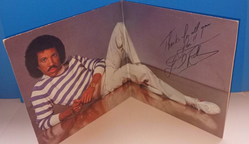 May include: Album cover featuring a man in a striped shirt and white pants. The man is lying down, with a signature and the words "Thanks for all you Love!!" written on the cover. The album is folded.
