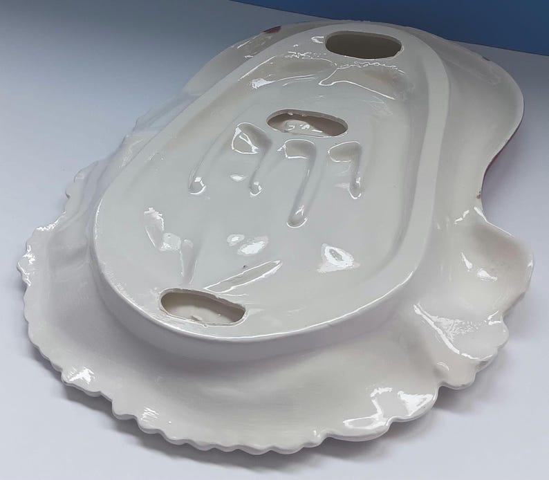 May include: A white ceramic serving dish with a scalloped edge. The dish has a unique shape with a raised center section and three oval cutouts. The underside is visible, showing the dish's form and design.