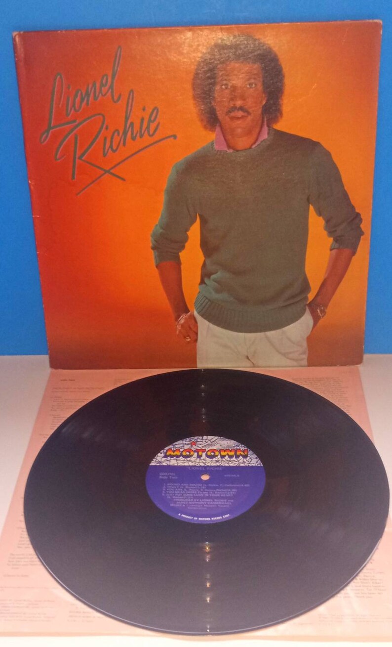 May include: Album cover featuring Lionel Richie in a green sweater and white pants against an orange background. The album title, "Lionel Richie," is in cursive. A vinyl record with a Motown label is in the foreground.