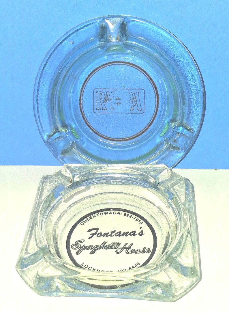 May include: Two clear glass ashtrays. The top round ashtray features a rectangular logo with the letters RA. The bottom square ashtray displays a circular label reading Fontana's Spaghetti House, Cheektowaga: 822-7918, and Lockport: 433-4446.