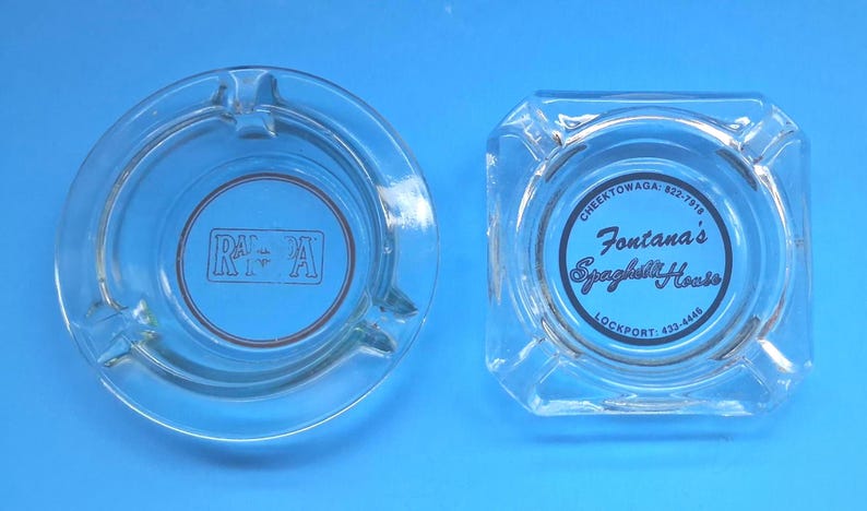 May include: Two clear glass ashtrays. The circular ashtray features a rectangular logo with the text RA-PA in the center. The square ashtray features a circular logo with the text Fontana's Spaghetti House, Cheektowaga: 822-7918, and Lockport: 433-4446.