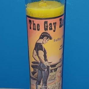 May include: A yellow candle in a clear glass jar. The label features a muscular man in a black shirt and jeans. Text on the label reads "The Gay R" and "Fully Adult Read".