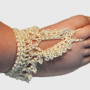 May include: Cream-coloured, crocheted barefoot sandals. The openwork design features a scalloped edge and a loop that fits around the big toe. The ankle bracelet style is connected to the toe loop with a delicate chain.
