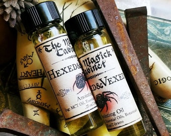 May include: Two small glass bottles with black caps and labels. The labels are white with black text and a spider graphic. The text on the labels reads "HEXED & VEXED" and "Anointing Oil, Essential Oils, Botanicals". The bottles are sitting on a rustic wooden surface with rusty nails.