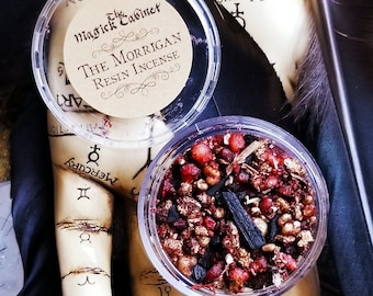 May include: A clear glass jar filled with a blend of red, brown, and black resin incense. The jar has a label that reads "The Morrigan Resin Incense" and "Magick Cabinet".