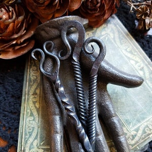 Iron nails twisted and shaped into a candle scribe resting on a black iron hand tarot cards under the hand.