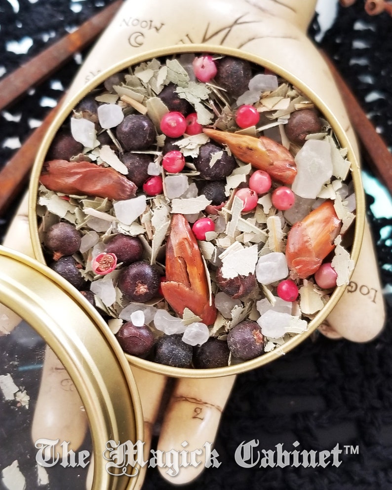 May include: A gold metal tin filled with a blend of herbs, spices, and crystals. The tin has a clear lid and the text "The Magick Cabinet&trade;" is printed on the bottom.