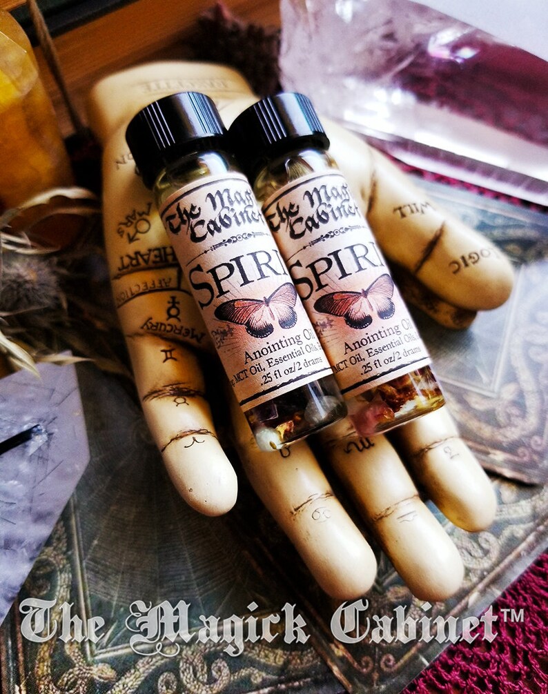 Spirit Guide oil in a 2 dram bottle. There's a lovely red butterfly on the label with the words The Magick Cabinet and Anointing oil. They stand on three tarot cards face down.