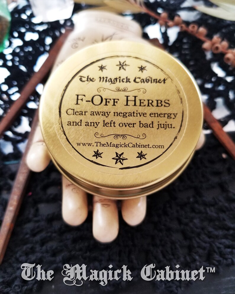 May include: A gold metal container with a black label that reads "The Magick Cabinet" and "F-OFF HERBS Clear away negative energy and any left over bad juju. www.TheMagickCabinet.com".