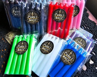 May include: Assortment of seven packs of small, thin, colored candles. Each pack contains four candles. The candles are packaged in clear plastic bags with a black and gold label that reads "Candle Magic". The colors of the candles are green, white, blue, red, pink, purple, and dark blue.