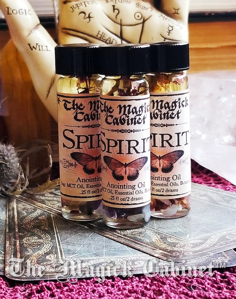 Spirit Guide oil in a 2 dram bottle. There's a lovely red butterfly on the label with the words The Magick Cabinet and Anointing oil. They stand on three tarot cards face down.
