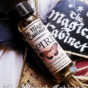 A single bottle of Spirit Guide oil laying on a old book tied with feathers and a page from a song book. The Magick Cabinet logo is in the background.