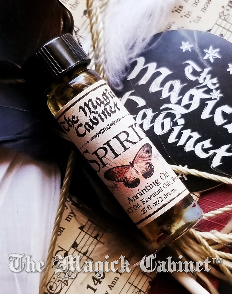 A single bottle of Spirit Guide oil laying on a old book tied with feathers and a page from a song book. The Magick Cabinet logo is in the background.