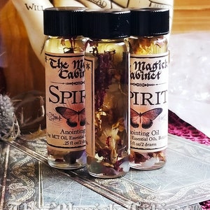 Spirit Guide oil in a 2 dram bottle. One of the bottles is turned around to show all the flowers and hers floating in the oil. The Magick Cabinet is on the label. They stand on three tarot cards face down.