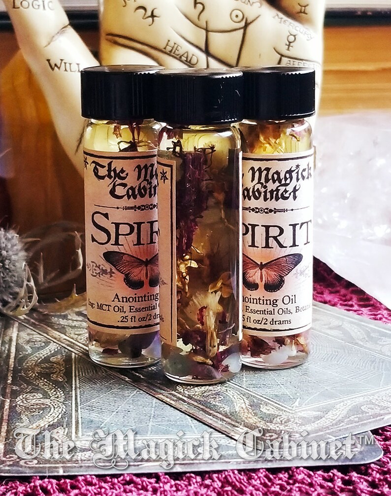 Spirit Guide oil in a 2 dram bottle. One of the bottles is turned around to show all the flowers and hers floating in the oil. The Magick Cabinet is on the label. They stand on three tarot cards face down.