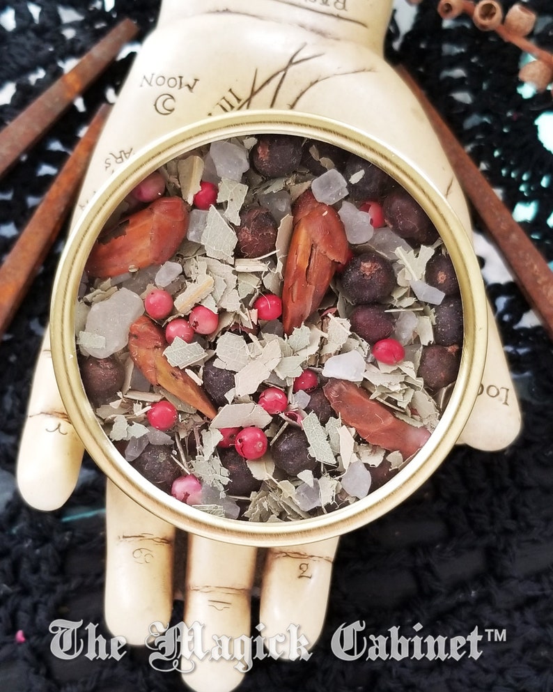 May include: A round metal tin filled with a mixture of dried herbs, spices, and berries. The tin is sitting on a hand with the words "The Magick Cabinet" written on the bottom.