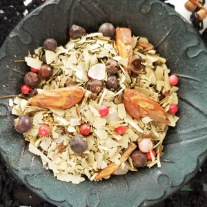 May include: A black bowl filled with a mixture of dried herbs, spices, and berries. The mixture includes dried leaves, pink Himalayan salt, red peppercorns, and juniper berries. The bowl is labeled "The Magick Cabinet TM".