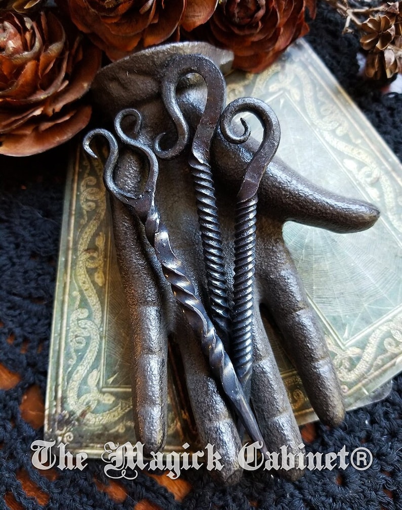 Iron nails twisted and shaped into a candle scribe resting on a black iron hand tarot cards under the hand.