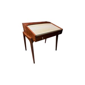 May include: A wooden writing desk featuring a slanted top with a white tambour roll-top cover. The desk has a single horizontal drawer with a small metal pull handle and is supported by four tapered legs that extend outward from the main body.