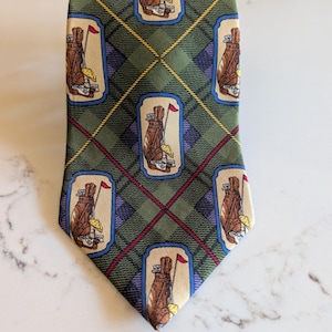 May include: Green plaid necktie with repeating golf bag and flag illustrations. The tie features a repeating pattern of brown golf bags with golf clubs and a red flag on a beige background, set against a green, blue, and burgundy plaid.