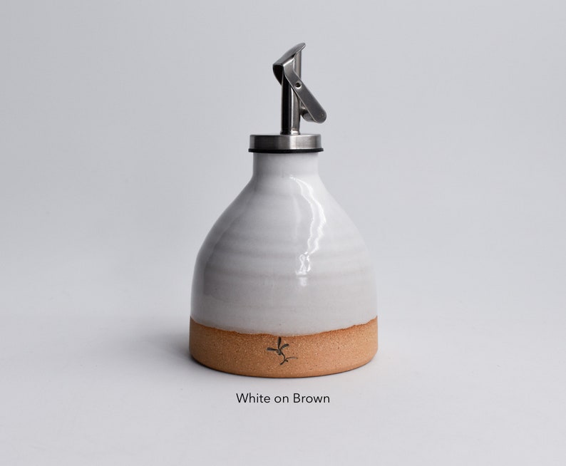 May include: White ceramic oil and vinegar bottle with a brown base and a stainless steel pour spout. The bottle is labeled "White on Brown".