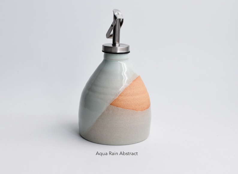 May include: A ceramic oil and vinegar bottle with a stainless steel pour spout. The bottle is glazed in a light blue and beige color with a peach-colored accent.