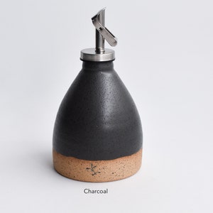 May include: A charcoal gray ceramic oil and vinegar bottle with a stainless steel pour spout and a speckled brown base.