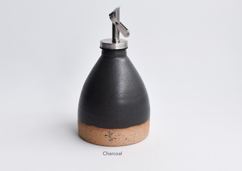 May include: A charcoal gray ceramic oil and vinegar bottle with a stainless steel pour spout and a speckled brown base.