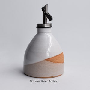 May include: White ceramic oil and vinegar bottle with a brown and beige abstract design. The bottle has a stainless steel pour spout with a lever.