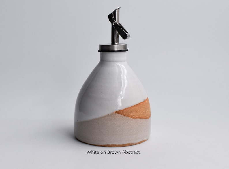May include: White ceramic oil and vinegar bottle with a brown and beige abstract design. The bottle has a stainless steel pour spout with a lever.