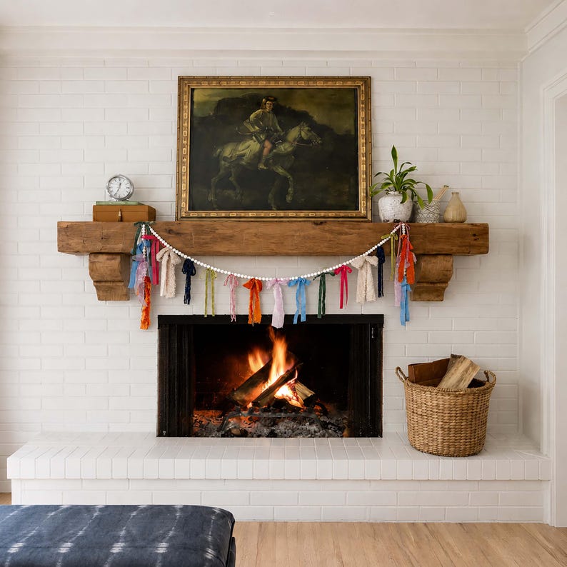 May include: A fireplace with a white brick surround and a wooden mantel. A garland of colourful fabric strips and white beads hangs above the fireplace. A painting of a person on a horse hangs above the mantel.