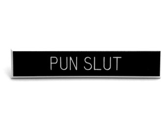 May include: Black rectangular desk nameplate with white text that reads "PUN SLUT".