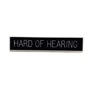 Peut inclure: Un panneau rectangulaire noir avec du texte blanc qui dit "HARD OF HEARING".