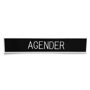 Puede incluir: Una placa negra con la palabra "AGENDER" en blanco, centrada. La placa tiene un borde plateado fino y está sobre un fondo blanco.