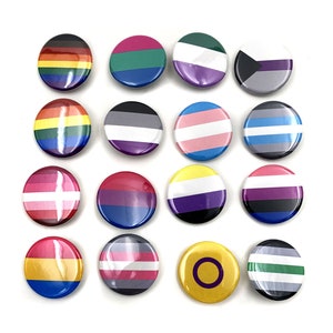 May include: Set of 15 round button badges featuring various pride flags, including the rainbow, transgender, bisexual, lesbian, and genderqueer flags.