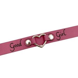 May include: A pink leather choker with a silver heart-shaped charm and the words "Good Girl" engraved on it.