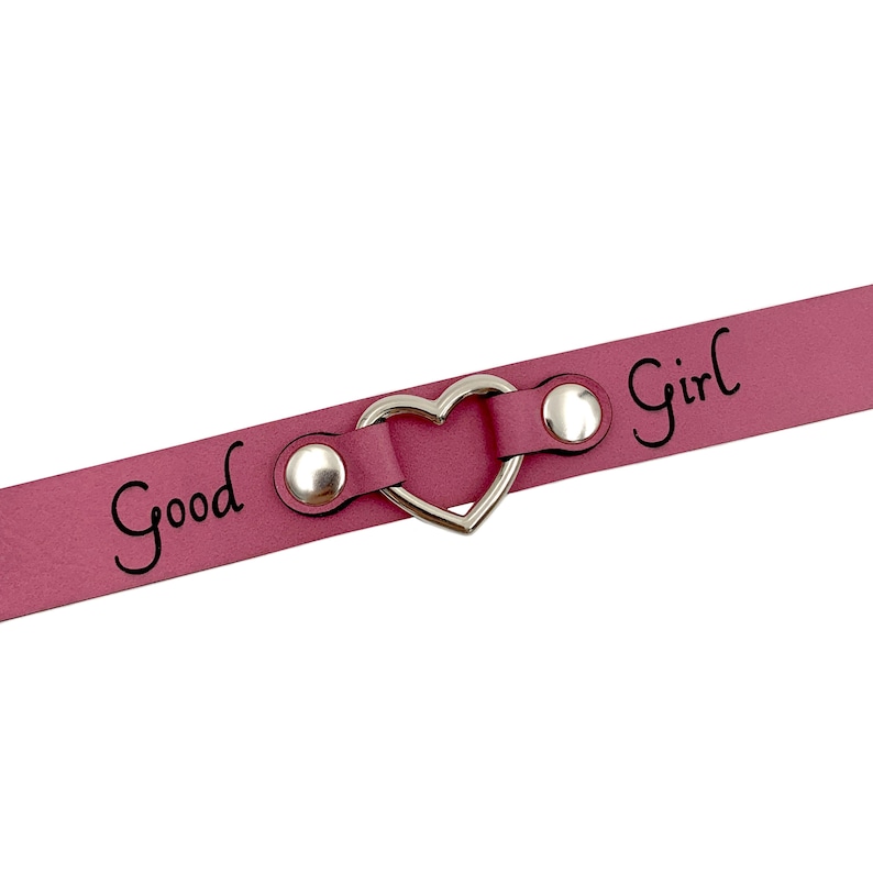 May include: A pink leather choker with a silver heart-shaped charm and the words "Good Girl" engraved on it.