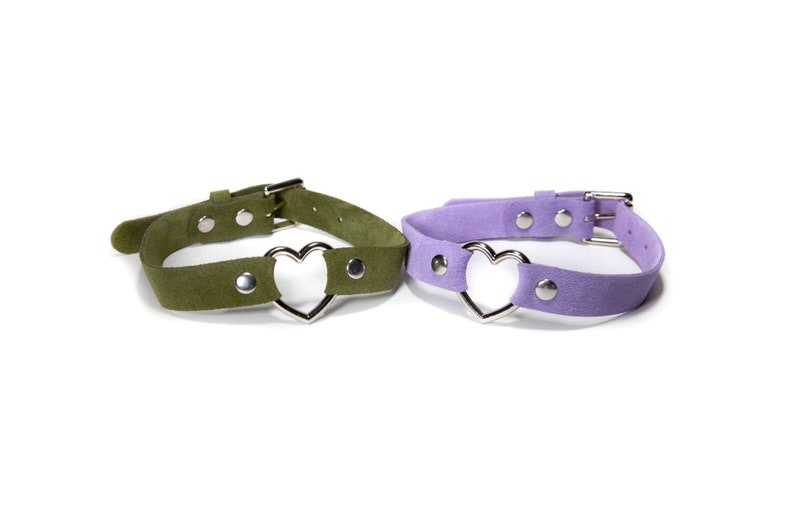 May include: Two suede choker necklaces with silver heart charms. One choker is green and the other is purple.