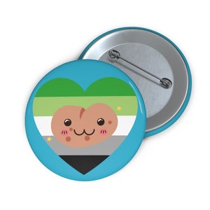 May include: A round, light blue button with a heart-shaped design featuring the aromantic pride flag colors: green, white, gray, and black. A cartoon potato character with a smiling face is in the center. A second button is visible in the background.