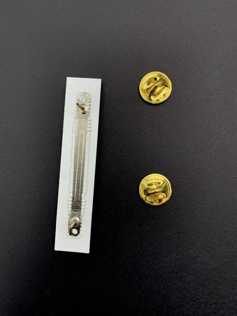 May include: The back of a white pin back with a silver clasp and two gold metal pin backs.