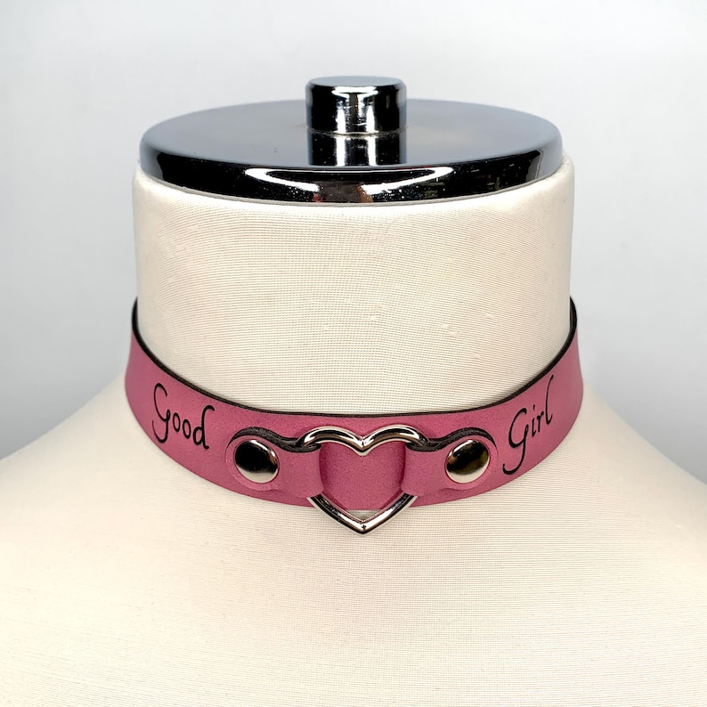May include: Pink leather choker with a heart-shaped metal accent and the words "Good Girl" engraved on the front.