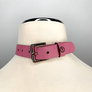 May include: A pink leather choker with a silver buckle and a small black circle logo that says "LAP".